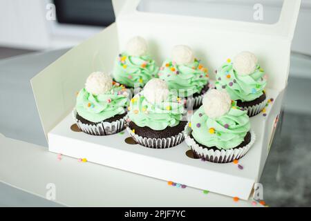 scatola bianca. Il pasticciere professionale preparò tortini sotto forma di alberi di Natale. Dolci deliziosi per ogni vacanza, regalo. Panna montata verde. Foto Stock