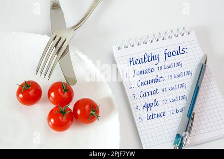 Pomodori ciliegini su un piatto con posate. Notebook per la registrazione e il conteggio delle calorie alimenti dietetici Foto Stock