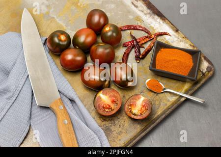Pomodori rossi, pepe macinato in una ciotola e cialde di pepe su un vassoio arrugginito Coltello e tovagliolo grigio. Sfondo grigio. Foto Stock