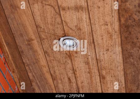 Un ritratto di un punto luce sigillato alle intemperie messo nelle tavole di legno di uno sbalzo del tetto. La lampada è spenta. Foto Stock