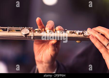 Un ritratto delle dita di una mano di un musicista flautista che stringe le valvole di un flauto d'argento metallico per suonare una nota di un brano musicale durante Foto Stock