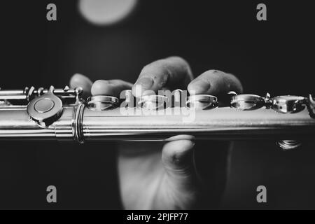 Un ritratto in bianco e nero delle dita di una mano di un musicista flautista che preme sulle valvole di un flauto d'argento metallico per suonare una nota Foto Stock