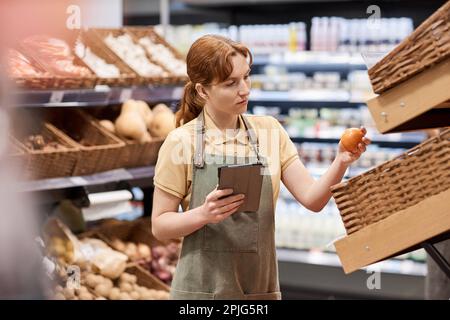 Vita in su ritratto di giovane donna che lavora in supermercato controllare i prodotti freschi in navata frutta e verdura Foto Stock