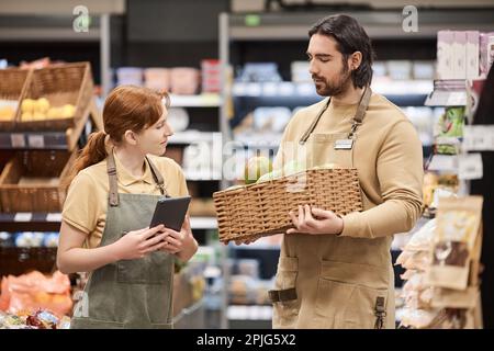 Vita in su ritratto di due giovani lavoratori in scaffali di stoccaggio supermercato con frutta fresca Foto Stock