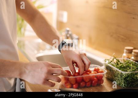 Primo piano della mano umana prendere pomodori ciliegini rossi in cucina Foto Stock