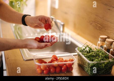 Primo piano della mano umana prendere pomodori ciliegini rossi in cucina Foto Stock