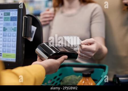 Primo piano di una giovane donna che utilizza terminale bancario a pagamento per alimentari in supermercato, copia spazio Foto Stock