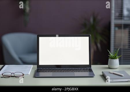 Immagine di sfondo di un computer portatile aperto con schermo bianco mockup sulla scrivania in elegante ambiente ufficio decorato con piante Foto Stock