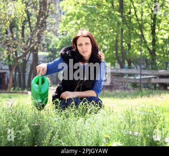 Donna vestita casual felice in giardino acque erbe e si prende cura Foto Stock