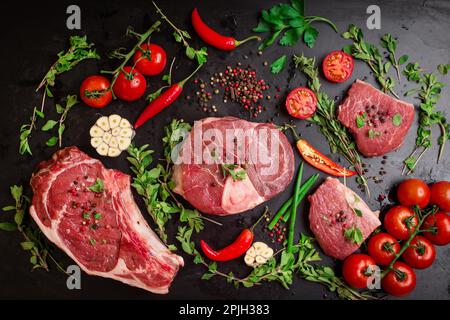 Diversi tipi di bistecche. Carne cruda assortita su un fondo di gesso nero. Costola occhio bistecca sull'osso, gambo di vitello (ossobuco), filetto con Foto Stock