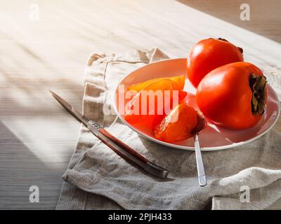 fette di persimmon in un piatto su un tavolo di legno. Foto Stock