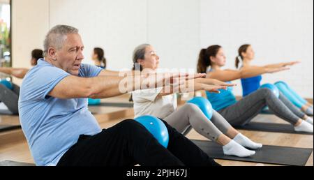 Uomo anziano che fa sit-up con la palla pilates in palestra Foto Stock