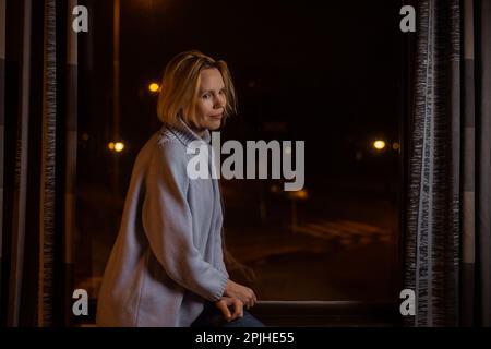 Una donna irriconoscibile siede sola in una stanza buia. Riflessioni, depressione, pensieri pesanti, concetto di solitudine. Foto Stock