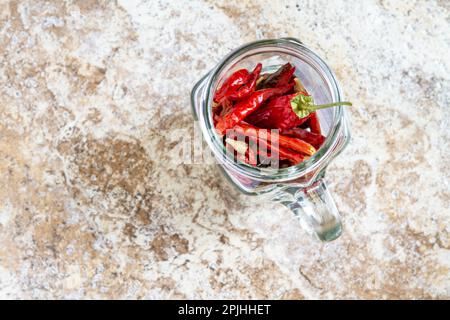 Guardando giù ad un vaso di vetro pieno di peperoni secchi di cayenne rossi luminosi (Capsicum annuum) su uno sfondo con un sacco di spazio di copia. Foto Stock