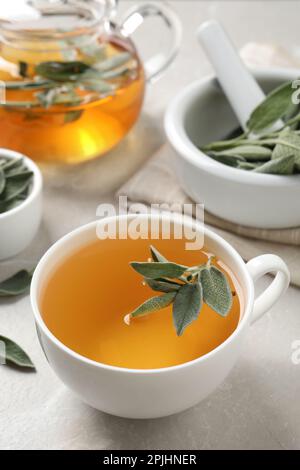 Tazza di tè di salvia con foglie verdi sul tavolo bianco Foto Stock