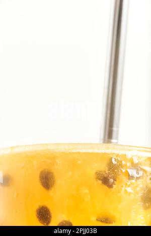 Primo piano della parte superiore di un bicchiere di una rinfrescante bevanda gialla di frutto della passione, succo o cocktail, con una cannuccia metallica ecologica riutilizzabile. Foto Stock