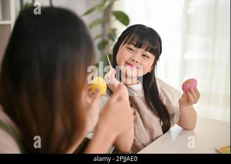 Una ragazza asiatica adorabile ama dipingere le uova di Pasqua con la madre in cucina. Foto Stock