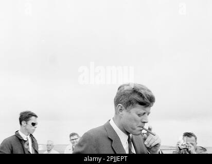 ST-250-16-6311 Maggio 1963President John F. Kennedy fumando un sigaro a Hyannis Port, Massachusetts; un fotografo e uomini non identificati guardano sopra. Si prega di accreditare “Cecil Stoughton. Fotografie della Casa Bianca. John F. Kennedy Presidential Library and Museum, Boston” Foto Stock