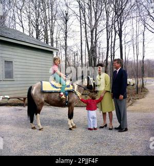 KN-C27672 31 Marzo 1963 Weekend a Camp David. Il presidente John F. Kennedy e la famiglia osservano Caroline Kennedy cavalcando un cavallo chiamato 'Macaroni' a Camp David. 'Maccheroni' indossa una sella marocchina blu e dorata, un regalo al presidente Kennedy dal re Hassan II La fotografia include: (L-R) Caroline Kennedy, John F. Kennedy, Jr., First Lady Jacqueline Kennedy, e il presidente Kennedy. Camp David, Maryland. Si prega di accreditare 'Robert Knudsen. Fotografie della Casa Bianca. John F. Kennedy Presidential Library and Museum, Boston' Foto Stock