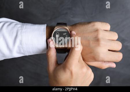 Orologio da polso elettronico di controllo da giovane con interfaccia Smart Home su sfondo grigio, primo piano Foto Stock