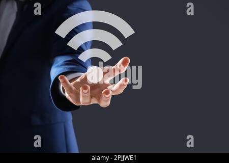 Uomo con simbolo Wi Fi in mano su sfondo grigio scuro, primo piano Foto Stock