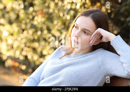 Donna penitente che contempla sedersi su una panchina al tramonto in un parco Foto Stock