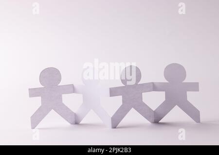 Primo piano di quattro fogli ritagliati persone figure tenendo le mani con spazio copia su sfondo bianco Foto Stock