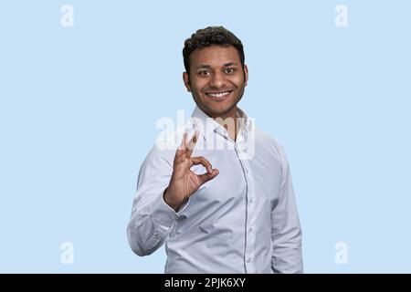 Felice giovane indiano mostra il segno di gesto OK. Isolato su sfondo blu pastello. Foto Stock
