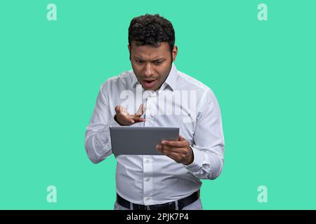 Ritratto di uomo indiano marrone arrabbiato con qualcuno online. Uomo d'affari con tablet pc su sfondo verde. Foto Stock