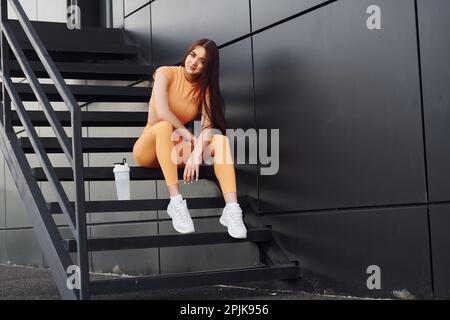 Siede sulle scale e contiene una bottiglia d'acqua. Giovane donna in abbigliamento sportivo hanno sessione di fitness all'aperto Foto Stock