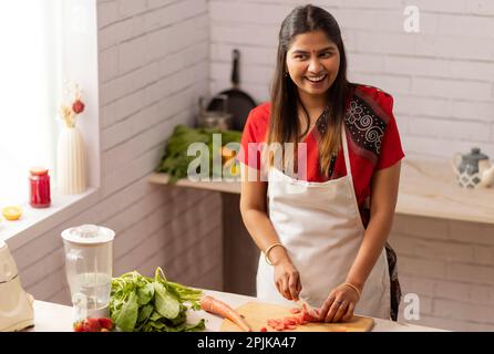 Donna sorridente tritare verdure in cucina Foto Stock