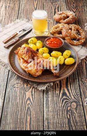 Hendl di pollo arrosto bavarese con patate bollite, servito con birra e primo piano di pretzel sul tavolo di legno. Verticale Foto Stock