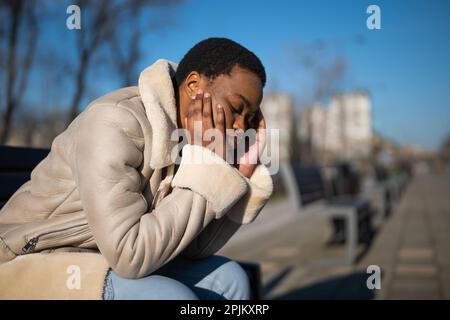 Ritratto all'aperto di depressa donna afro-americana in giornata di sole. È seduta su panca per strada. Foto Stock