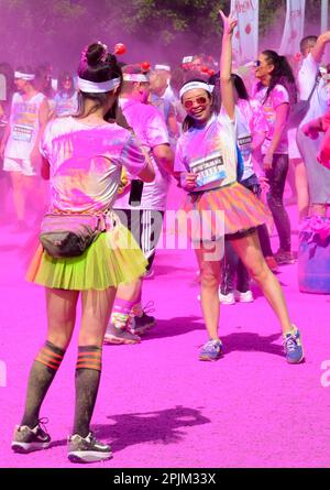 Corridori in posa a Colour Run UK a Birmingham indossando tutus e ricoperti di polvere di vernice con altri corridori visibili sullo sfondo Foto Stock