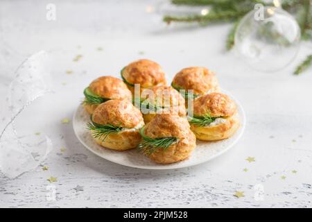 Profiteroles di formaggio con formaggio cremoso, cetriolo ed erbe aromatiche, gugere, dolci tradizionali francesi, in un piatto bianco su sfondo grigio chiaro, top vie Foto Stock