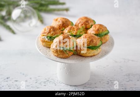 Profiteroles di formaggio con formaggio cremoso, cetriolo ed erbe aromatiche, gugere, dolci tradizionali francesi, in un piatto bianco su sfondo grigio chiaro, top vie Foto Stock