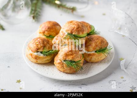 Profiteroles di formaggio con formaggio cremoso, cetriolo ed erbe aromatiche, gugere, dolci tradizionali francesi, in un piatto bianco su sfondo grigio chiaro, top vie Foto Stock