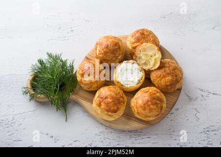 Profiteroles di formaggio con formaggio cremoso, cetriolo ed erbe aromatiche, gugere, dolci tradizionali francesi, in un piatto bianco su sfondo grigio chiaro, top vie Foto Stock