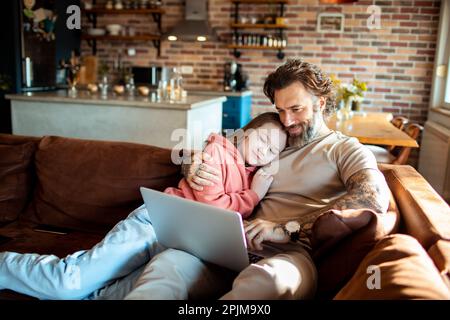 Primo piano di un padre e di una figlia che utilizzano un computer portatile su un divano in un soggiorno Foto Stock Primo piano di un padre e di una figlia che utilizzano un computer portatile su un divano in un soggiorno Foto Stock