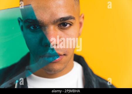 Uomo millenario che guarda intensamente la telecamera e che copre il suo volto con un filtro verde su sfondo giallo. Foto di alta qualità Foto Stock