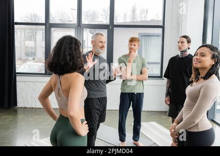 Allenatore di mezza età che parla con la gente interracial in studio di yoga, immagine stock Foto Stock