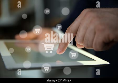 Concetto di consegna. Uomo che utilizza un tablet moderno per lo shopping online in interni, primo piano. Illustrazioni del carrello di mercato Foto Stock