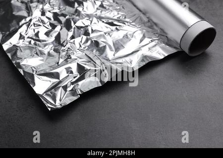 Rotolo di foglio di alluminio su tavolo grigio scuro, primo piano Foto Stock