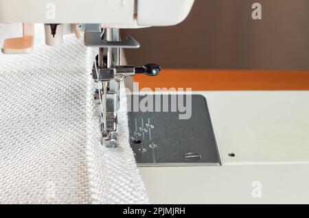 Moderno piedino pressatore per macchina da cucire. il processo di cucitura di un bordo decorativo di stoffa bianca. Foto Stock