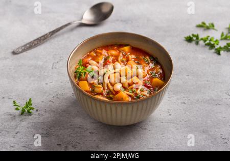 Minestrone italiano di stagione vegano con zucca, fagioli, pomodori, peperoni, pasta ed erbe su fondo grigio. Delizioso fo fatto in casa Foto Stock