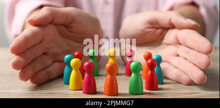Donna che protegge pedine colorate a tavola di legno, primo piano. Concetto di diversità e inclusione Foto Stock