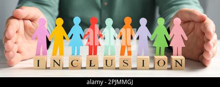 Donna che protegge pedine colorate e cubi di legno con parola inclusione a tavola bianca, primo piano. Design del banner Foto Stock