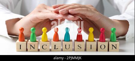 Donna che protegge pedine colorate e cubi di legno con parola inclusione a tavola bianca, primo piano. Design del banner Foto Stock