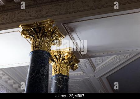 Colonne di pietra con capitelli color oro sono sotto il soffitto bianco, foto di sfondo di architettura classica Foto Stock