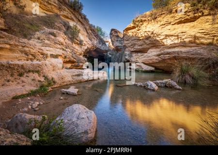 Bellissimo ambiente di una cascata chiamata Salto del Utro a Bullas, Murcia, Spagna. Acque blu e cristalline sotto una grotta di roccia gialla Foto Stock